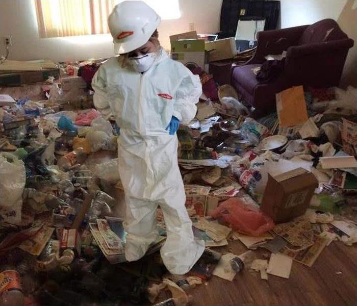 girl dressed in white hazmat suit standing in very messy room