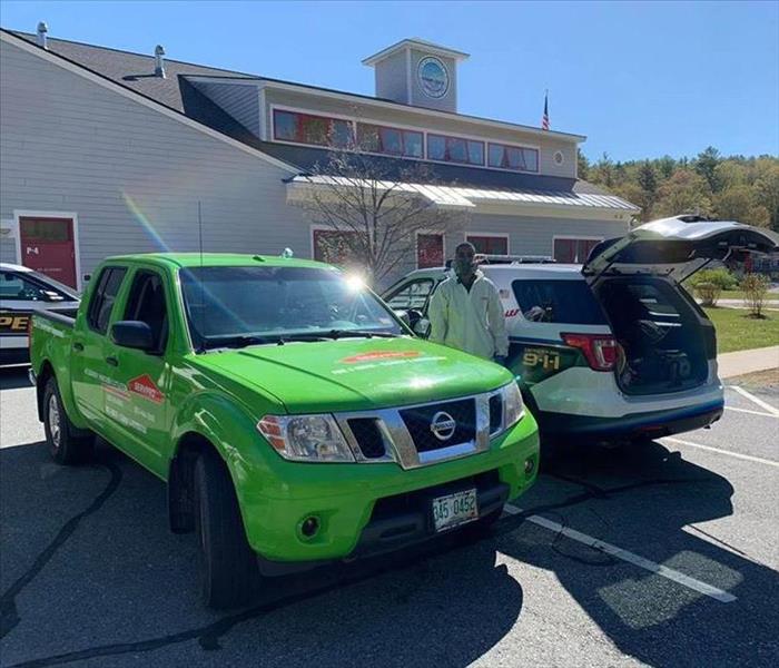 picture of SERVPRO tech standing by a police car and SERVPRO truck after cleaning cars