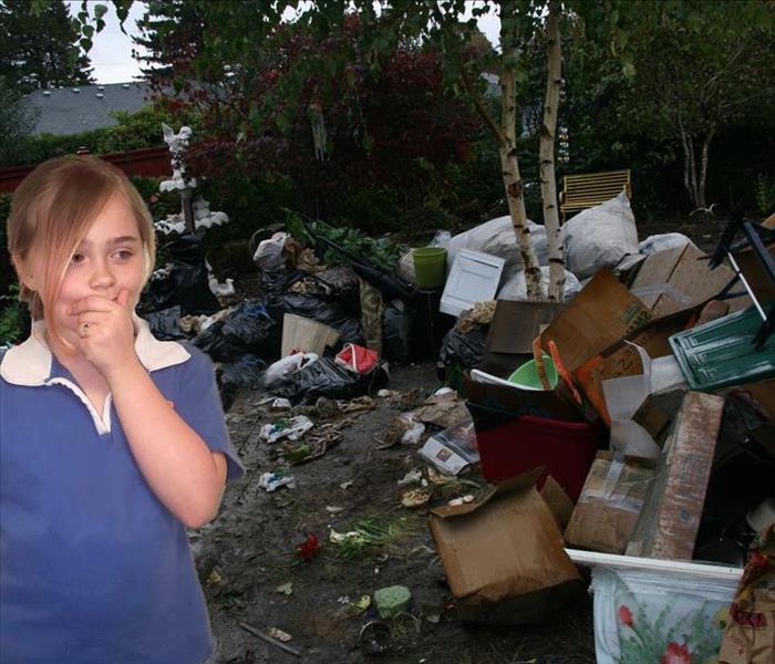girl standing outside in front of piles of garbage and junk