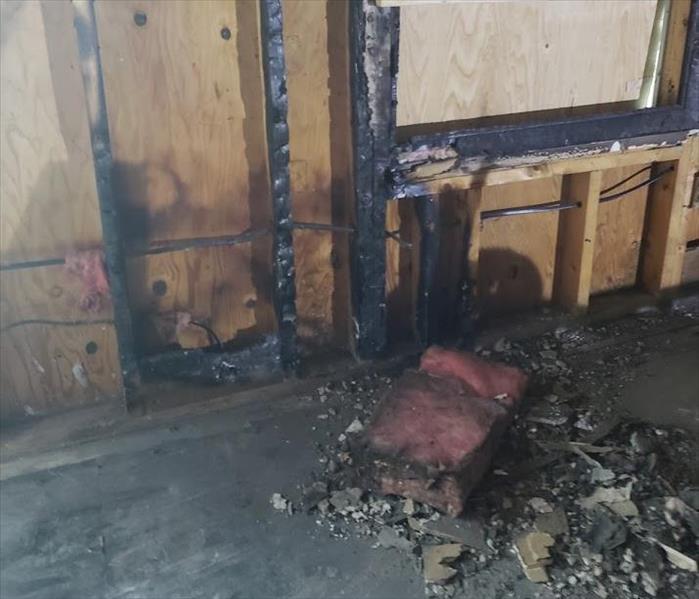 a room with fire damaged wood framing and burnt insulation and rubble on floor