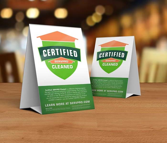 Table tent signs describing the Certified: SERVPRO Cleaned program on top of a wooden table.